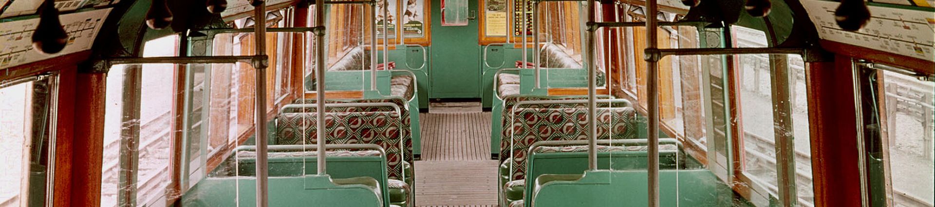 1938 tube stock carriage interior. The carriage is empty with not people. Either side of the aisle in the centre of the carriage are moquette seats in a green fabric.