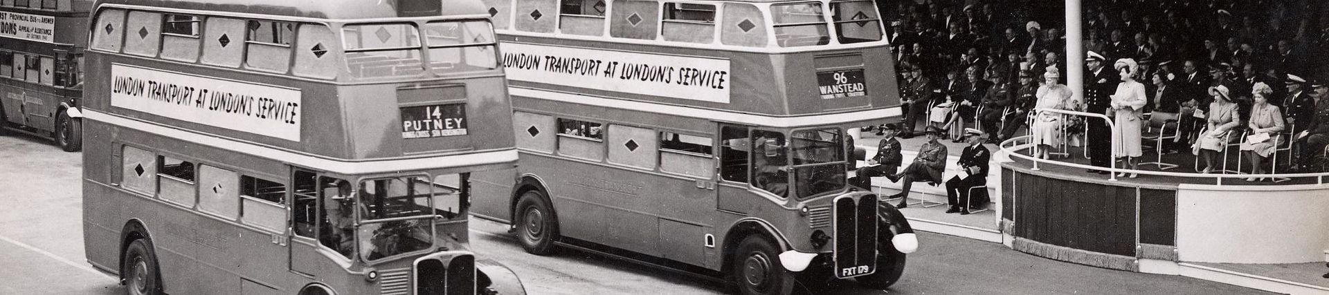 Black and White photography of two R.T. buses in the Victory Parade. The Royal family can be seen waving to them.