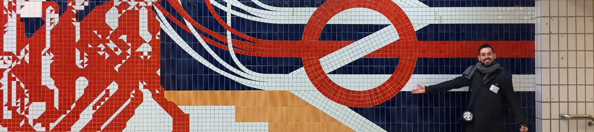 A photo of tile mosaic for the old King's Cross Thameslink entrance. The roundel inside the National rail symbol with red stylised people in the mosaic going down stairs
