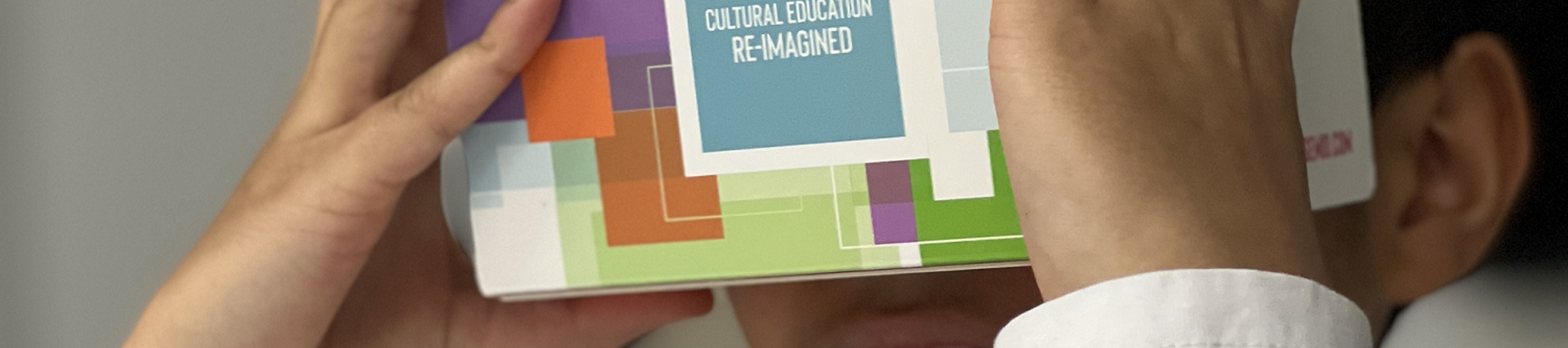 A photo of a child holding a coloured cardboard box up to his eyes with the words Cultural Education Reimagined on