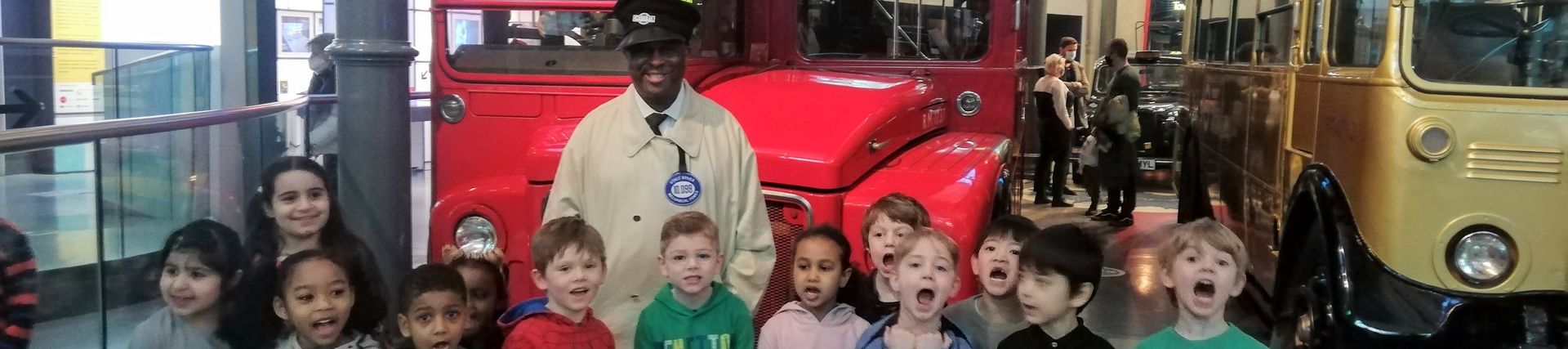A man dressed as a bus conductor and a group of school children pose in front of a bus in the museum