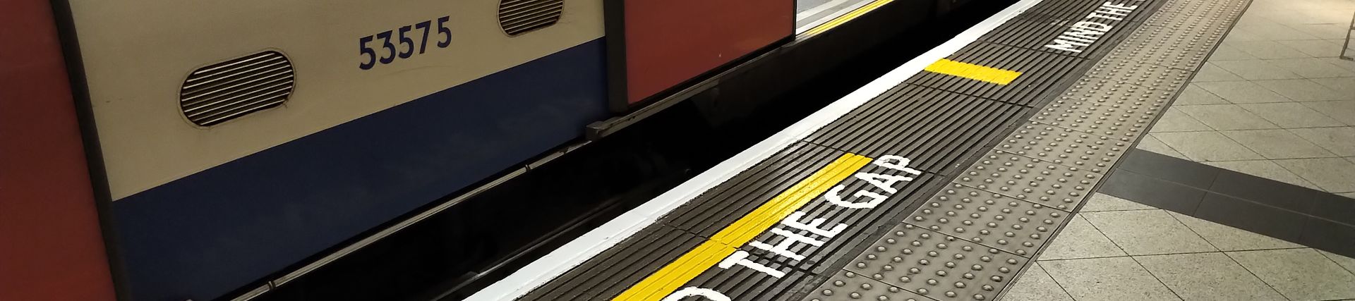 A Tube train along a platform with a yellow line and the words Mind the Gap