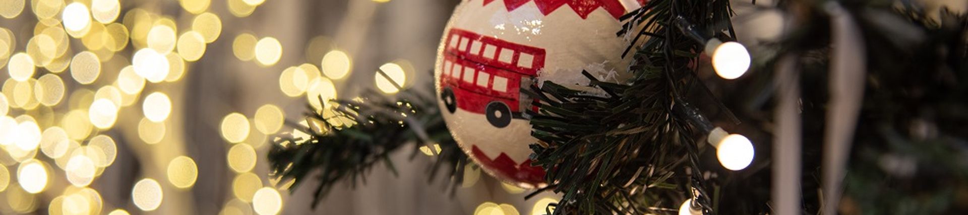 Christmas bauble with a red bus hanging on a Christmas tree in front of fairy lights